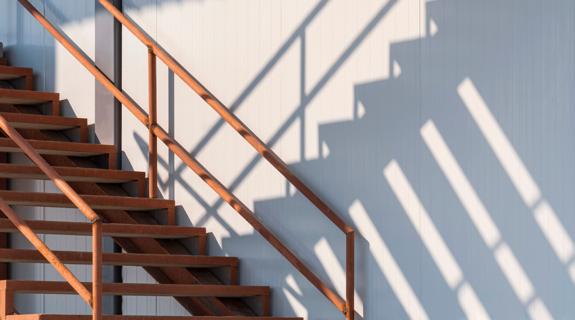 Rust-orange stairwell casting geometric shadows on a pale facade